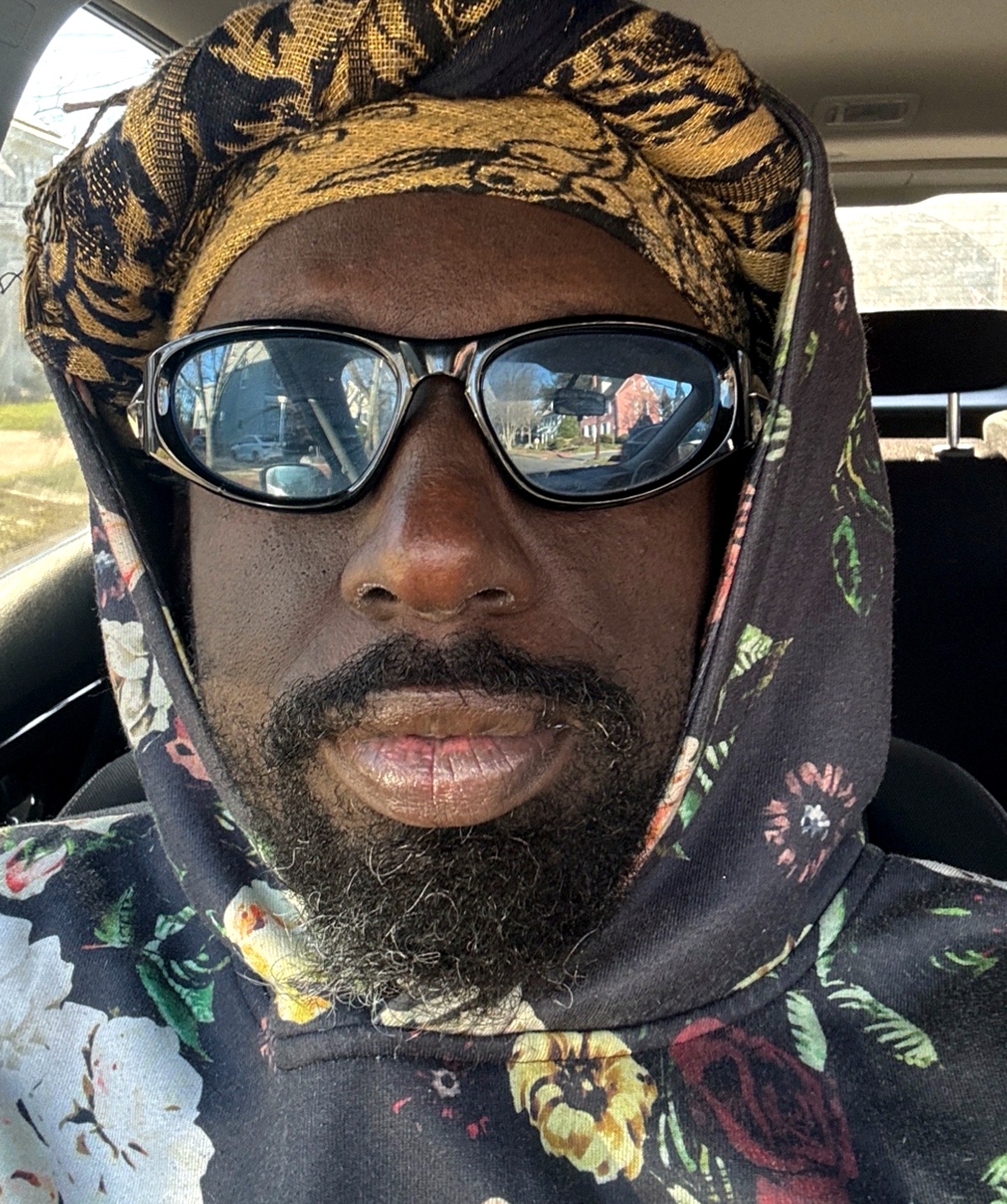 Portrait of Yasheen Vickers wearing sunglasses, a head wrap, and a floral hoodie.